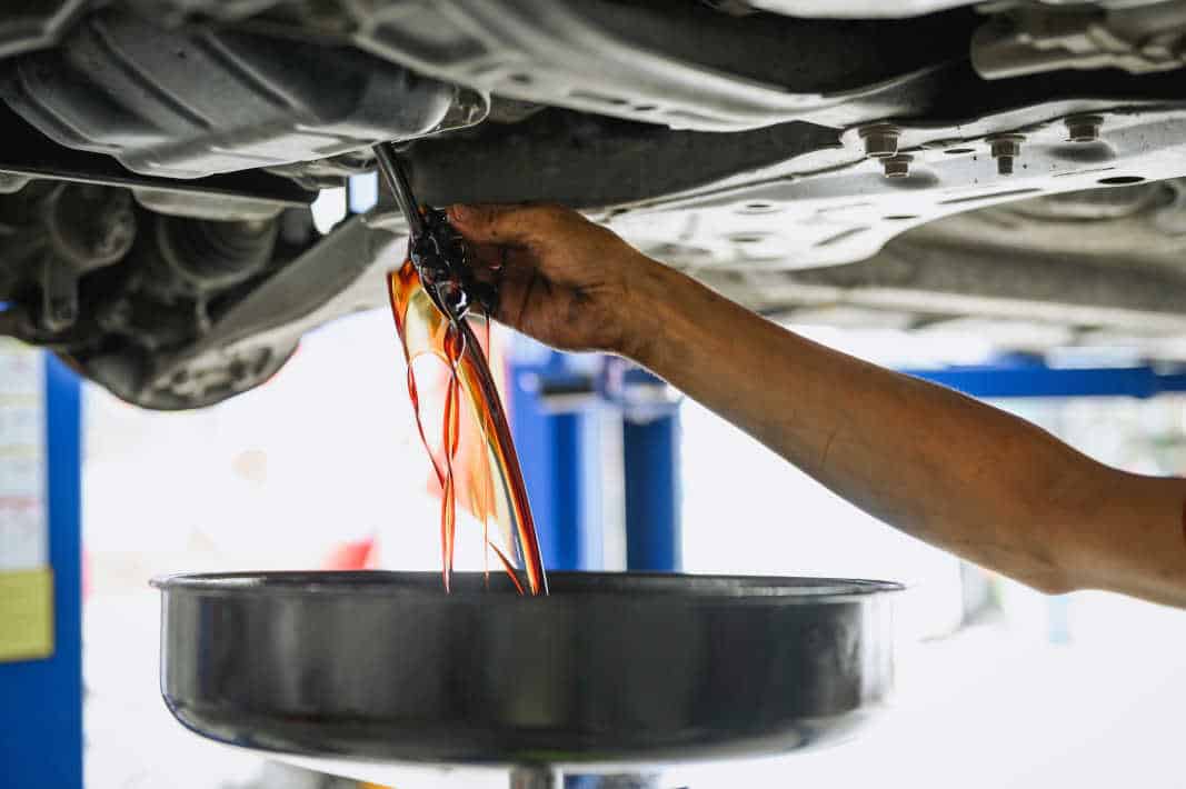 Auto mechanic draining dirty engine oil. Close-up of a mechanic draining oil during an oil change at Pulaski Automotive, ensuring engine performance and longevity.